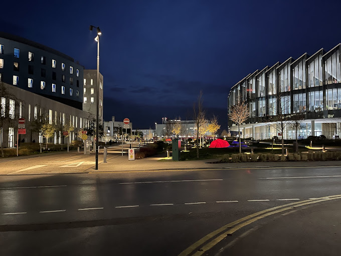Night view of a modern university campus with illuminated buildings, a sidewalk, and streetlights.