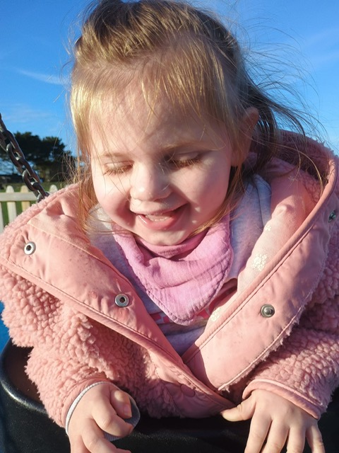 Sleeping toddler in patterned pajamas hugging a blue stuffed toy, lying on a pink blanket.